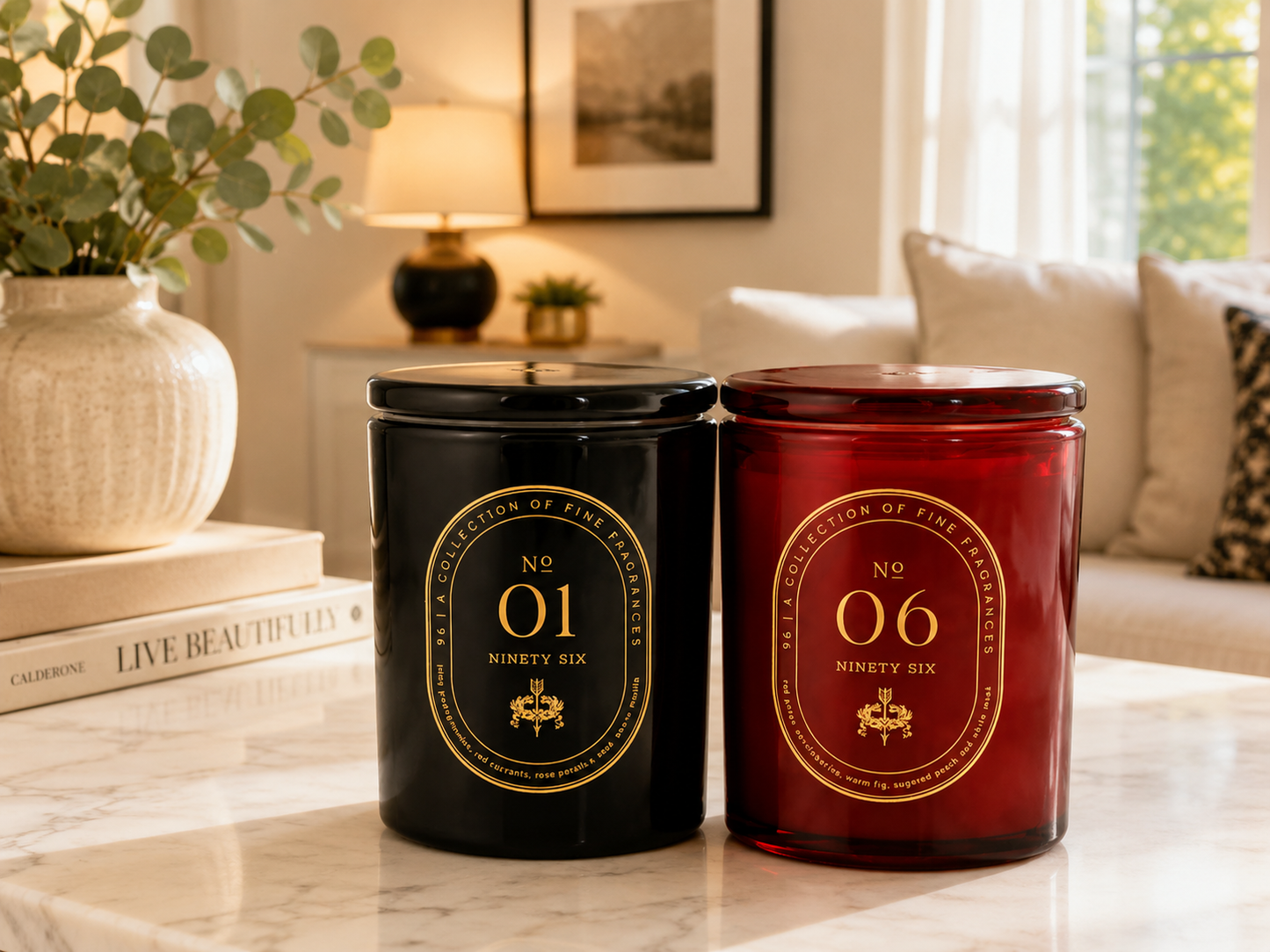 Two candles, one black and one red, with gold labels on a marble surface in a living room setting.